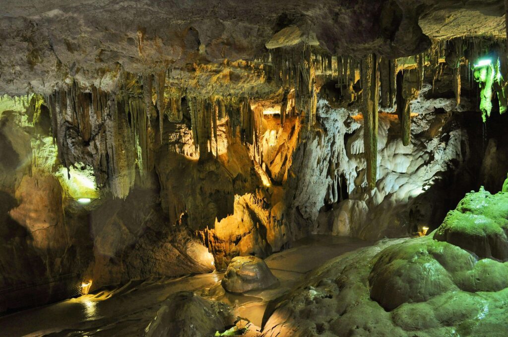 Stalactites and stalagmites inside a limestone cave illuminated by warm lighting, representing the type of ancient geological formations.