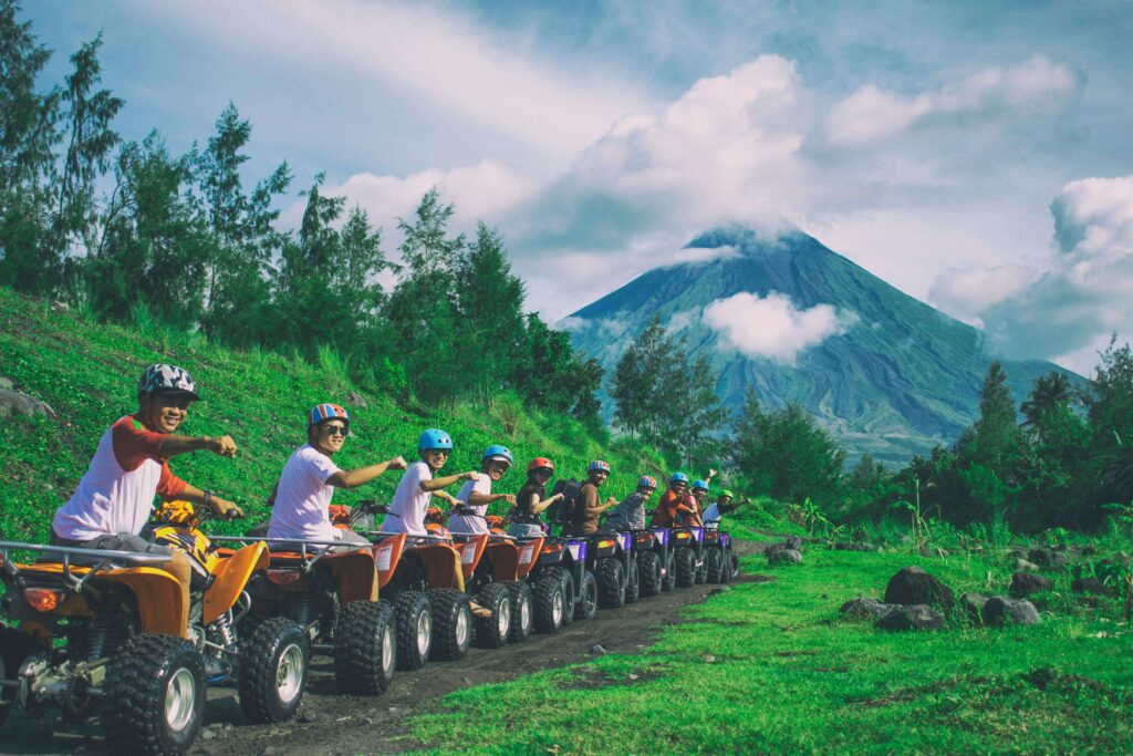 Group of ATV riders lined up on a green hillside with a cloud-wrapped volcano rising in the background, similar to views near Arenal Volcano in Costa Rica