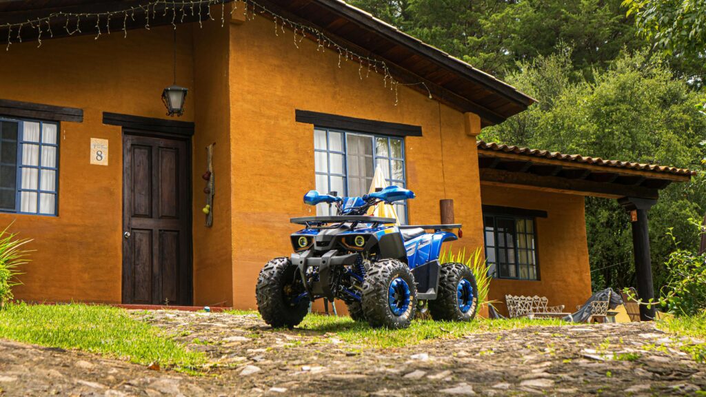 Blue ATV parked on green grass in front of a traditional orange-walled Costa Rica lodge with dark wooden doors