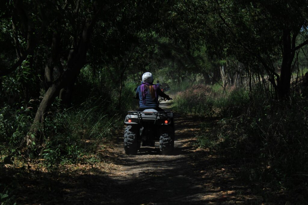 Rider wearing a white helmet driving an ATV down a shaded dirt trail through dense tropical forest in Costa Rica