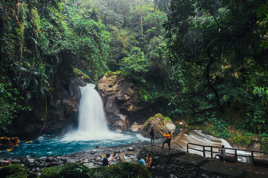 Visitors enjoy a rainforest waterfall with turquoise pools in Costa Rica's Central Highlands, similar to the five cascades along La Paz Waterfall Gardens' paved trail system