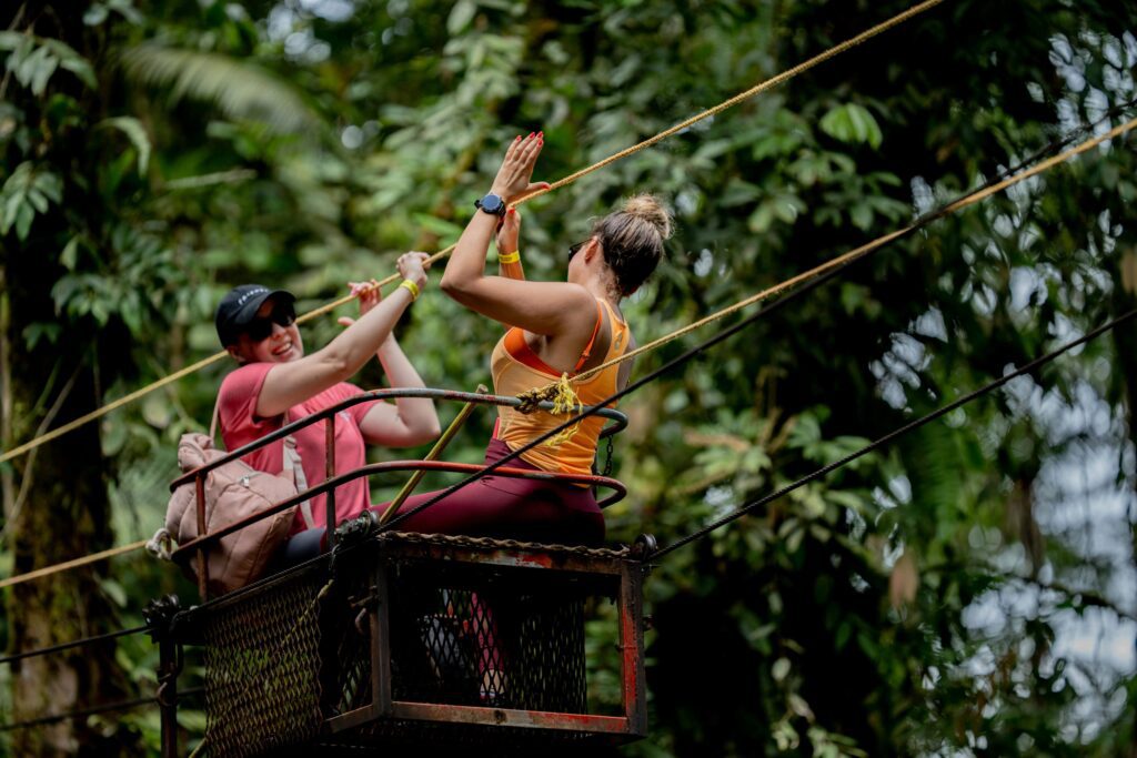 Two visitors high-fiving on a jungle aerial tram above Costa Rica rainforest canopy during an adventure tour