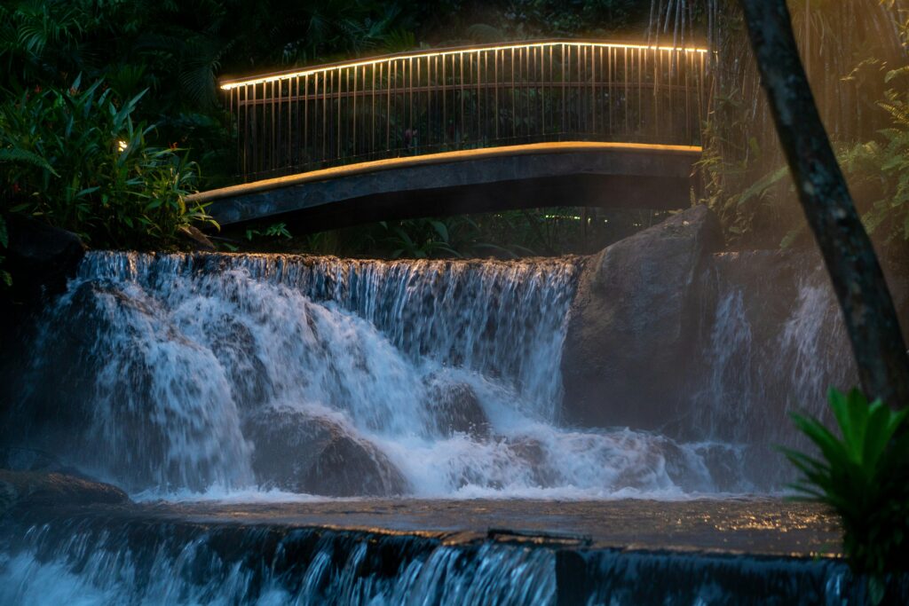 Lit bridge arching over cascading geothermal water at a Costa Rica hot springs resort at dusk
