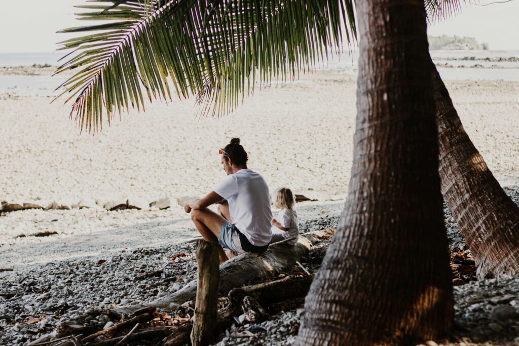 Similar to Costa Rica's remote island beaches — adult and child resting on driftwood along a secluded Pacific shoreline