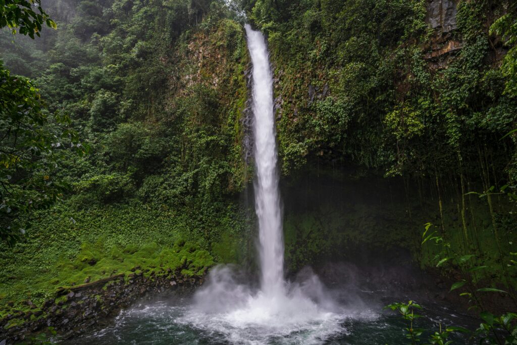 La Fortuna Waterfall plunging into a dark jungle pool surrounded by moss-covered volcanic cliffs in Costa Rica