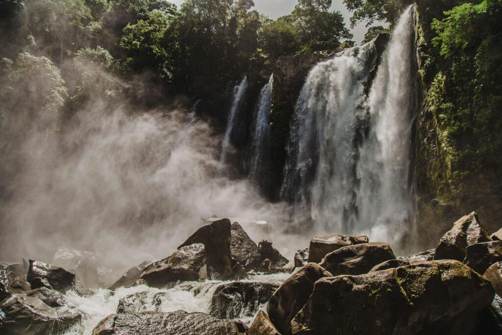 Misty spray rising from waterfall similar to Nauyaca Waterfalls over rocky riverbed in Costa Rica