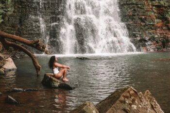 Visitor sitting on rock at waterfall swimming hole similar to Nauyaca Waterfalls near Dominical, Costa Rica