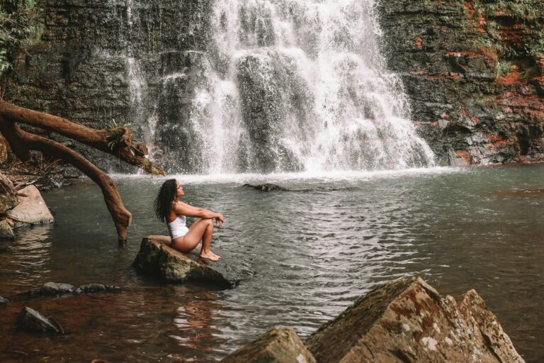 Visitor sitting on rock at waterfall swimming hole similar to Nauyaca Waterfalls near Dominical, Costa Rica