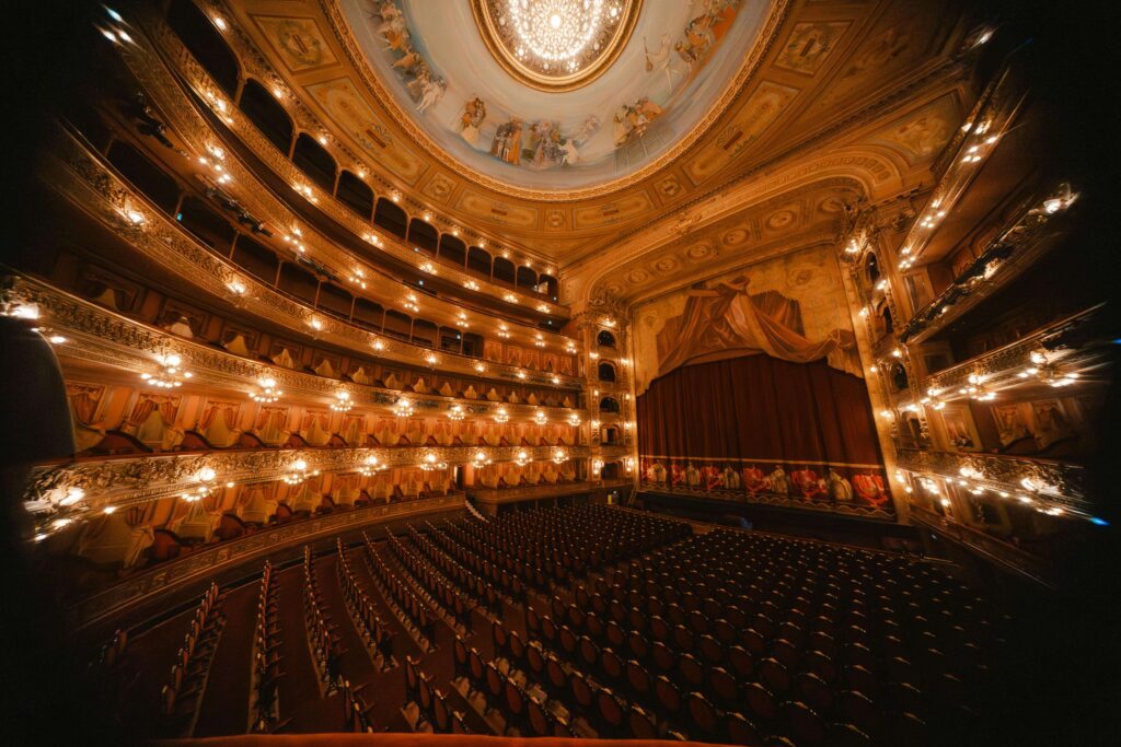 Grand interior of Teatro Nacional Costa Rica showing empty red velvet seats, multiple gilded balcony levels, chandeliers, and a painted ceiling dome
