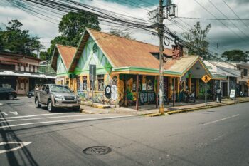 Street corner in Zarcero, Costa Rica, with colorful buildings, murals, and light traffic.
