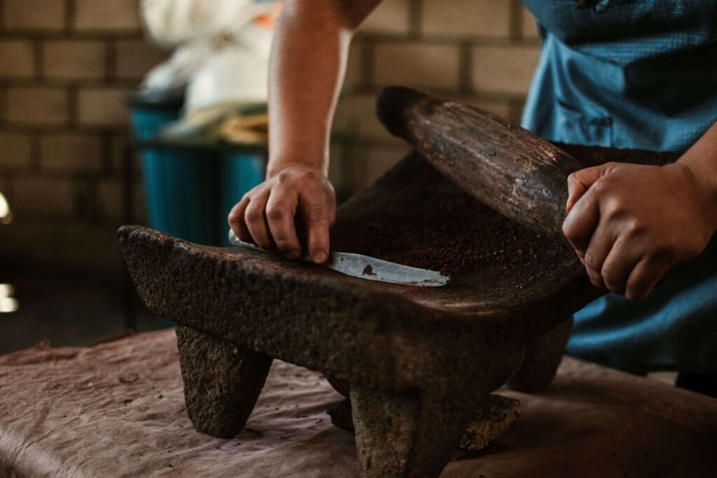 Hands grinding roasted cacao beans on a stone metate, similar to BriBri chocolate demonstrations in Costa Rica