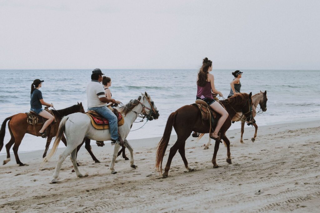 Guided group riding horses along the sand beside the surf, similar to a horseback tour from Montezuma to Playa Cocolito