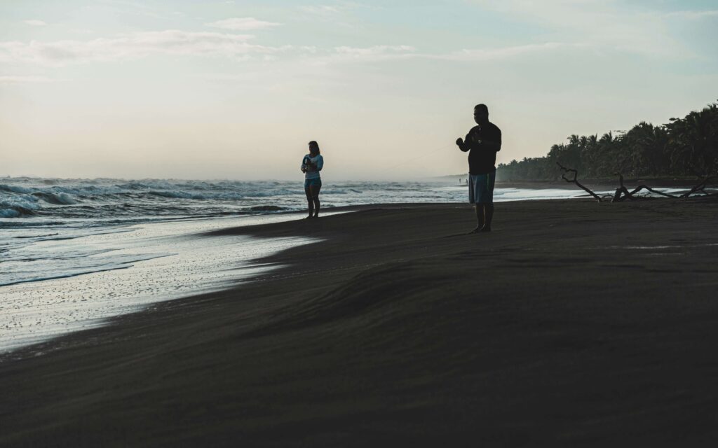 Two people standing on the beach near the waterline at dusk with palms along the shore, similar to Playa Cocles, Costa Rica