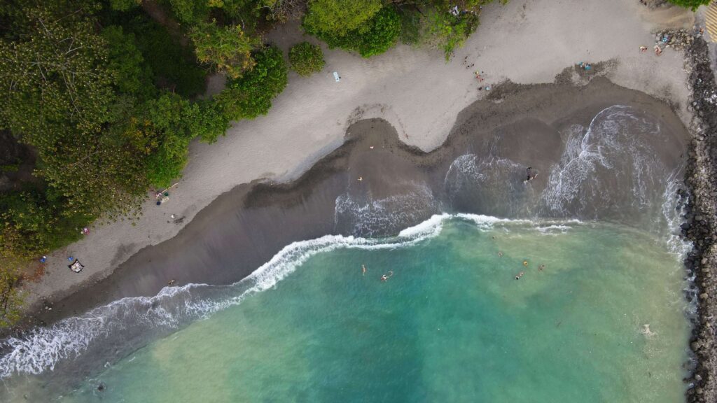 Aerial view of a wide sandy beach meeting turquoise water beside forest, similar to Playa Grande in Guanacaste, Costa Rica