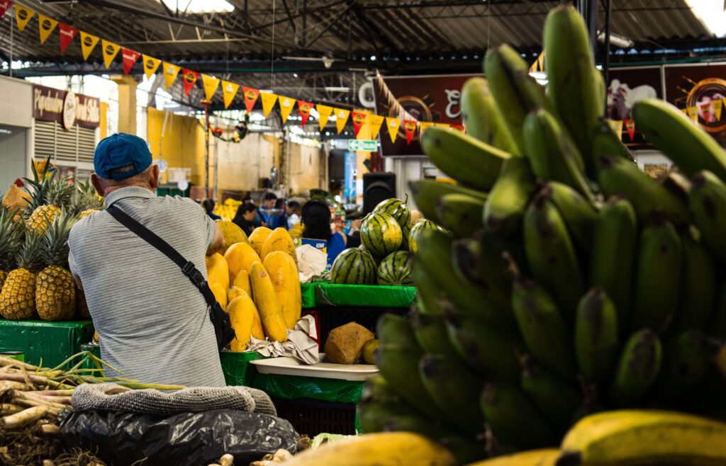 Vendor tending a stall of pineapples, papaya, and plantains under festive bunting, similar to San José Central Market, Costa Rica