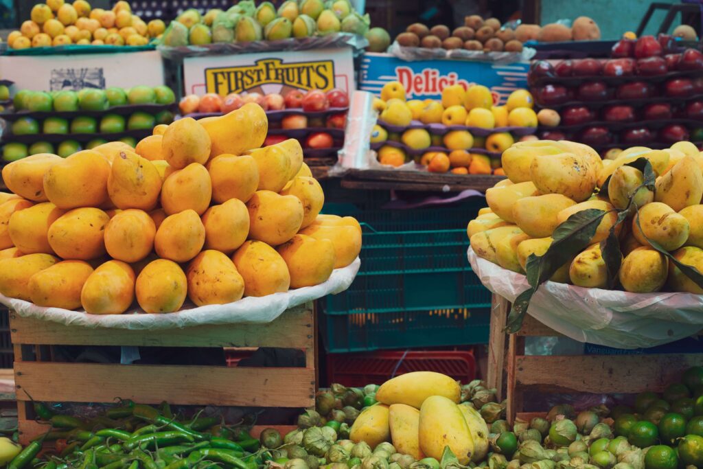 Market stall with piles of ripe yellow mangoes on crates above tomatillos, chiles, and limes, similar to San José Central Market, Costa Rica