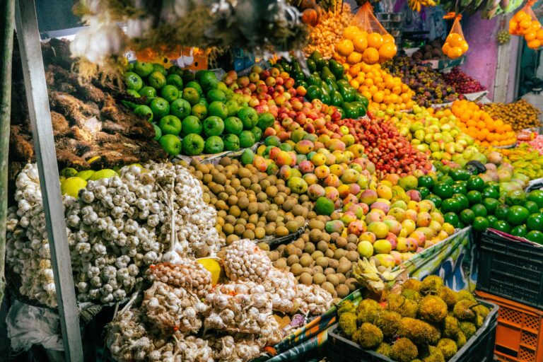 Market stall piled with tropical fruit, garlic braids, limes, and mamón chino, similar to San José Central Market, Costa Rica