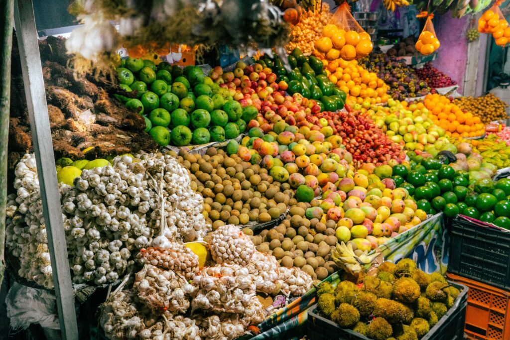 Market stall piled with tropical fruit, garlic braids, limes, and mamón chino, similar to San José Central Market, Costa Rica